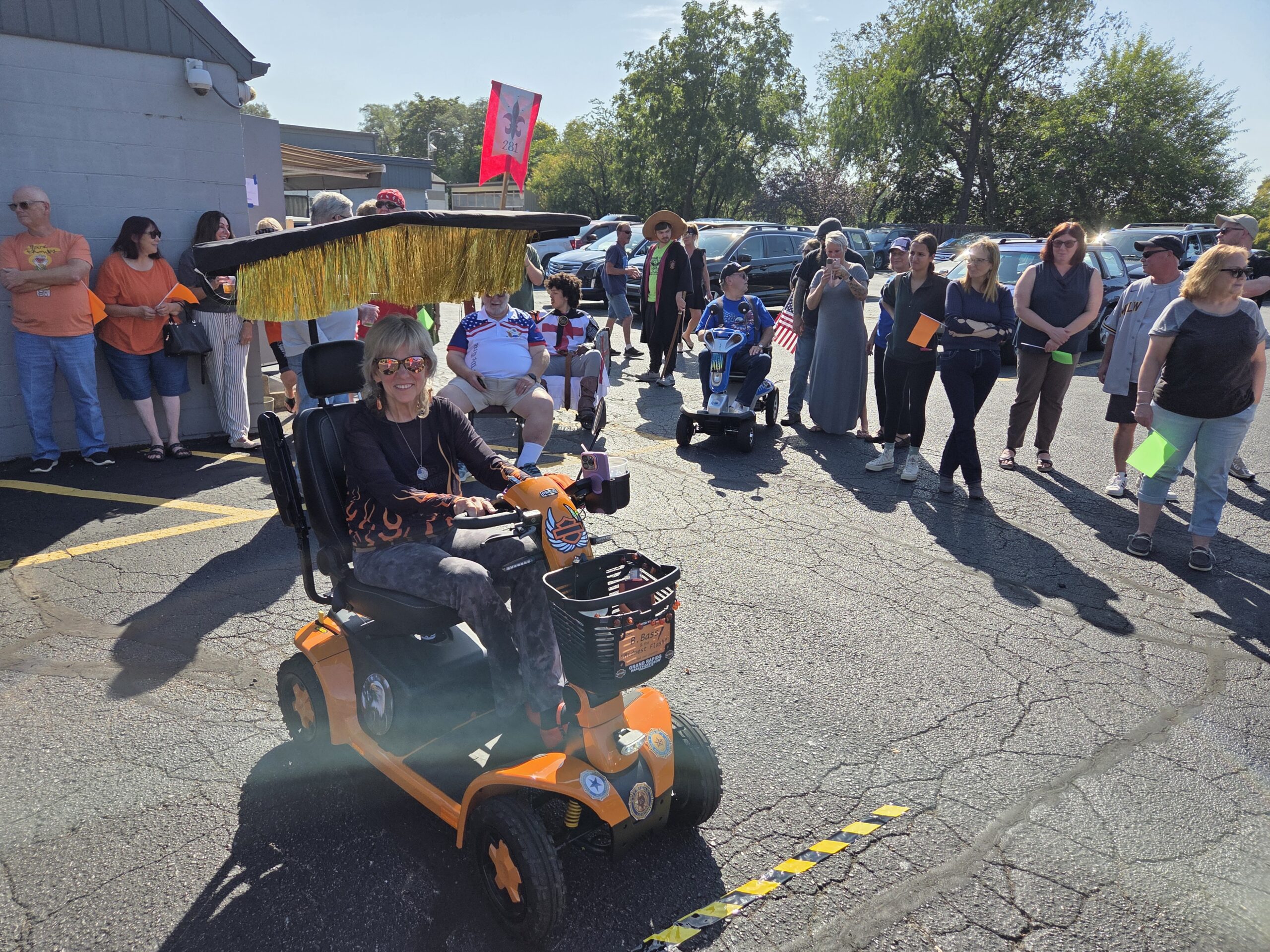 Victoria Mavis drives her decorated orange mobility scooter past a crowd at a One Day in the Chair disability awareness event.